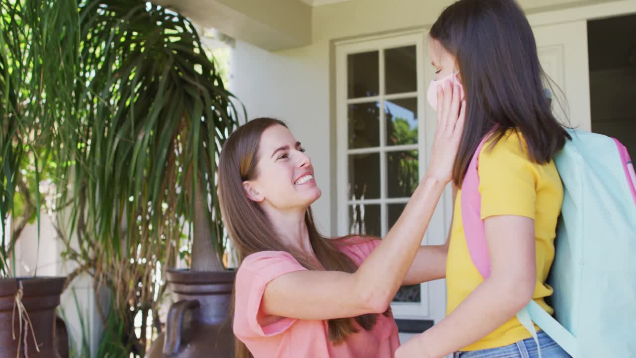백인 어머니가 얼굴 마스크를 쓰고 집 밖에서 딸을 안아주고 있습니다.