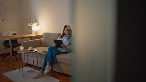 attractive woman looking tablet screen sitting sofa evening home. lady working