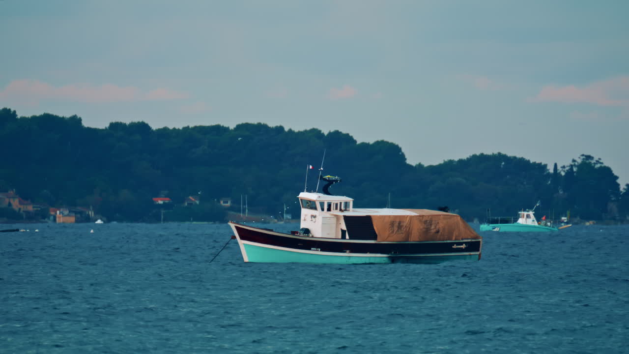 A wooden workboat with a brown tarp cover anchored on a windy sea