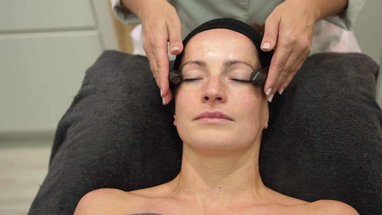 Esteticista massageando o rosto de cliente com cristais pretos