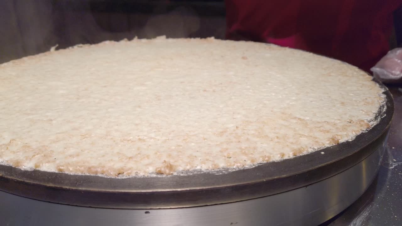Large crepe batter cooking on hot plate in indoor food market, warm and casual vibe