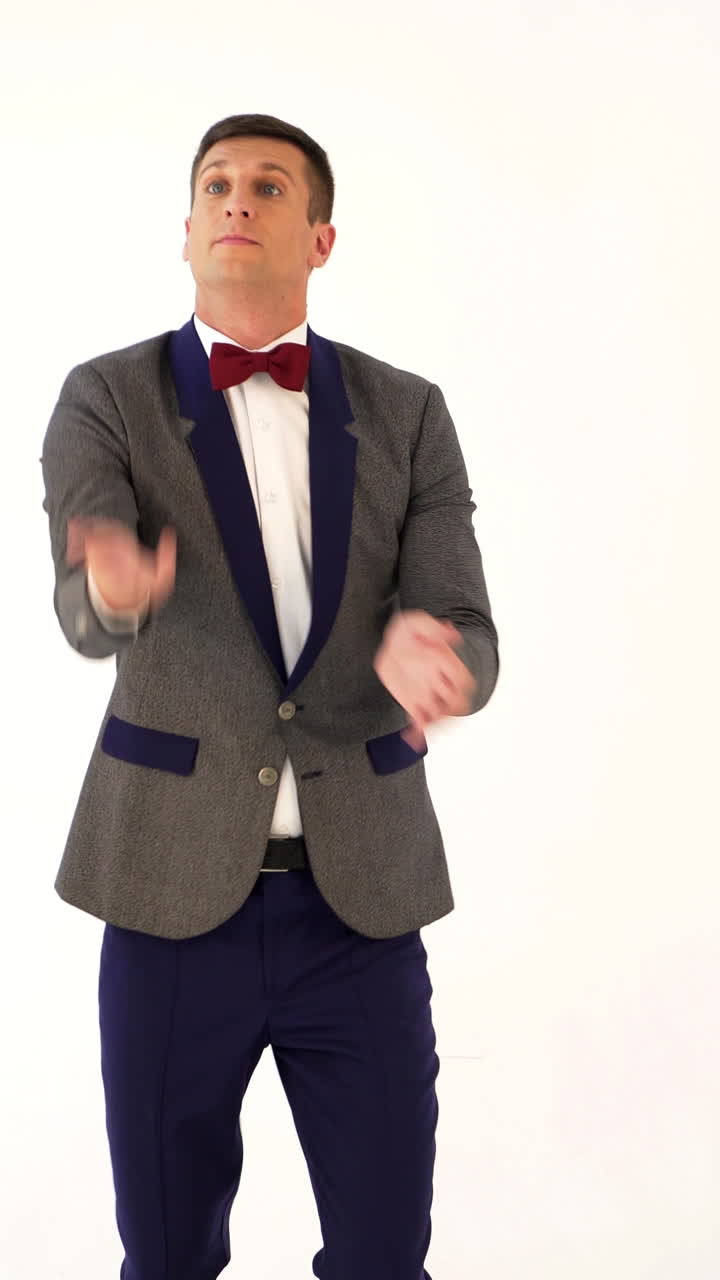 a man in a gray and blue colours of suit is juggling as a clown in the studio. Parody of a funny clown in a circus Vertical video