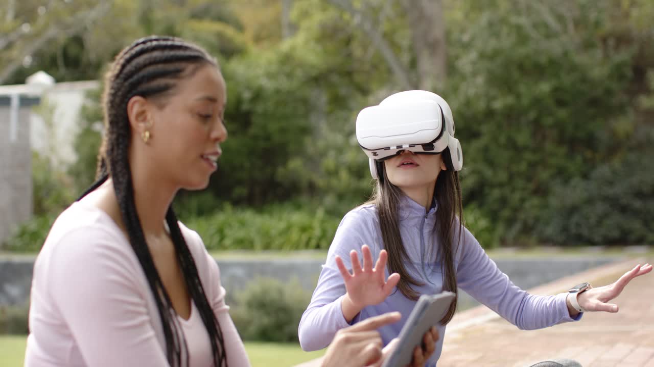 Diverse female friends starting VR headset using tablet prompt and exploring virtual world on patio