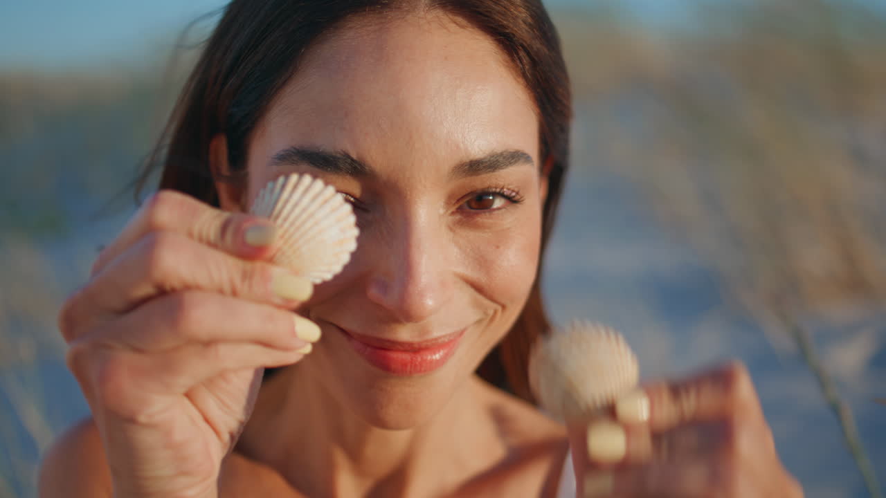 Modello giocoso che posa nella natura, coprendosi gli occhi con delle conchiglie in primo piano. Ritratto di donna