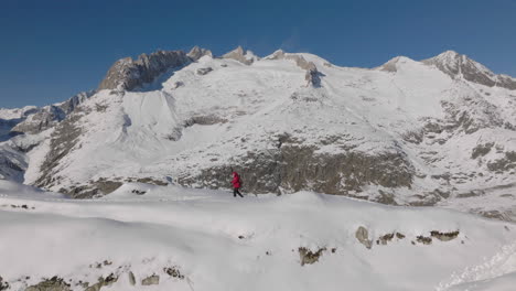 Aerial-shot-in-Switzerland-with-a-person-walking-with-snow-shoes-on-a-sunny-day-with-a-glacier-behind