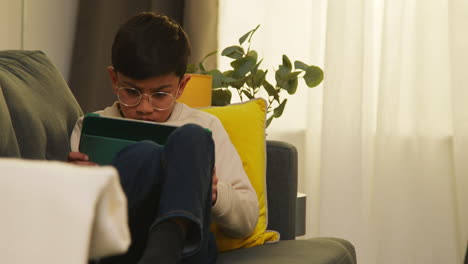 young boy sitting on sofa at home playing games or streaming onto digital tablet 1