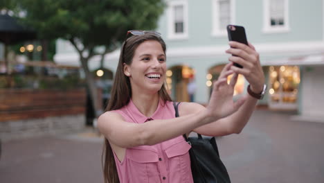 retrato en cámara lenta de una joven hermosa mujer sonriendo posando tomando una foto selfie usando un teléfono inteligente de fondo urbano