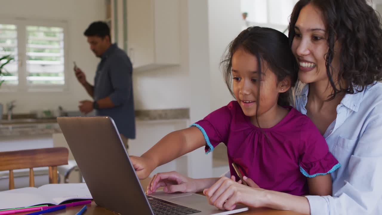 madre y hija hispanas felices sentadas en la mesa mirando la computadora portátil