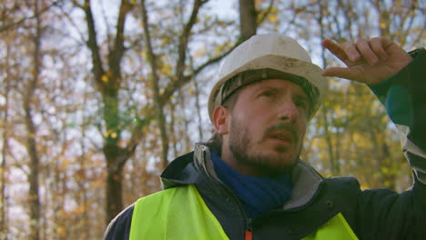 male engineer wearing hard hat staring upwards at the trees in the middle of the forest, handheld closeup