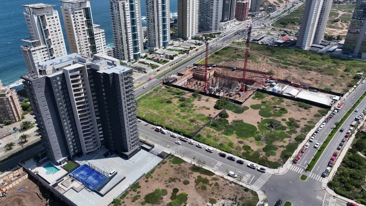 Forward revealing drone aerial of Viña del Mar coastal towers and construction cranes, Pacific Ocean backdrop, highway and urban development, Chile