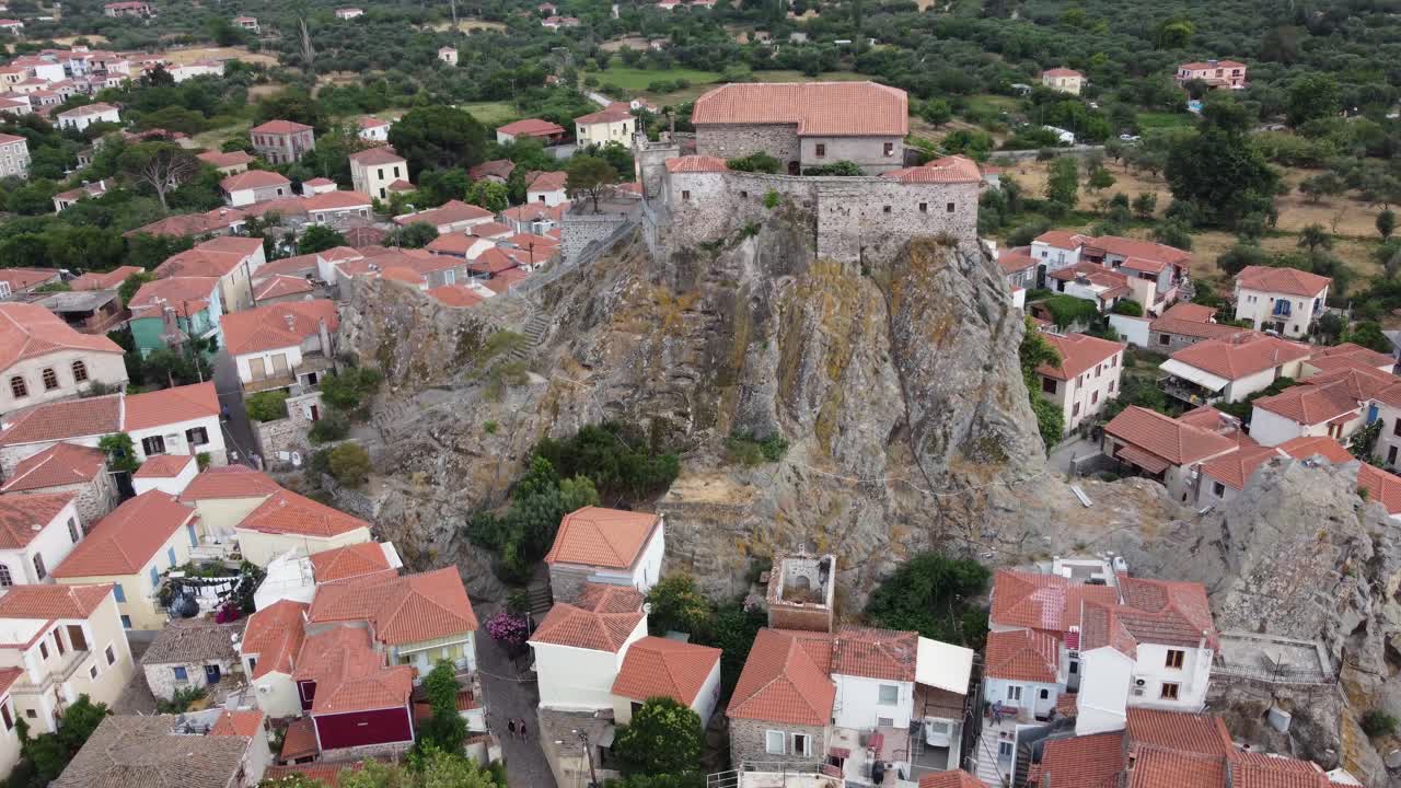 Virgin Mary Greek Orthodox church courtyard at top of rock surrounding Petra village traditional houses with terracotta roofs, Aegean Sea, Lesvos, Drone view