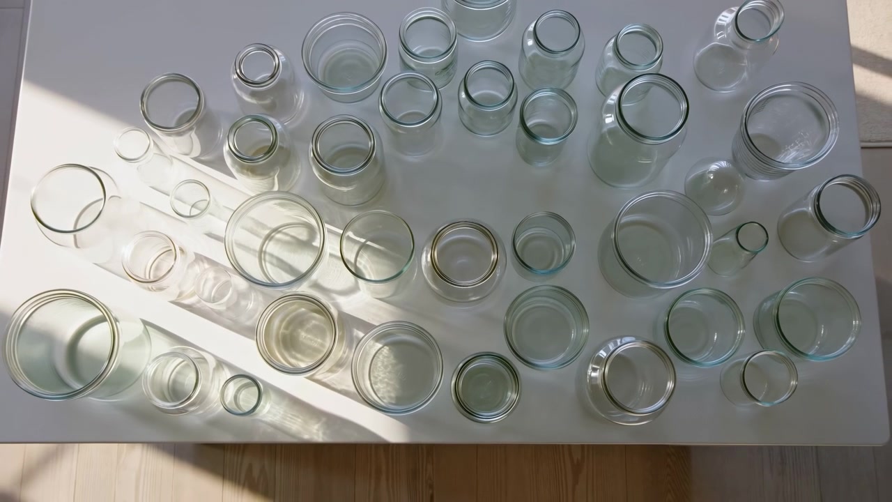 Glass beads are observed in a top-down indoor setting with natural light, creating a neutral and serene atmosphere. These clear and light green glass beads are displayed on a wooden surface.