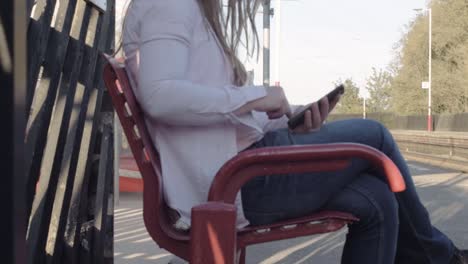 mujer usando un teléfono móvil mientras espera un tren en el andén de la estación de tren