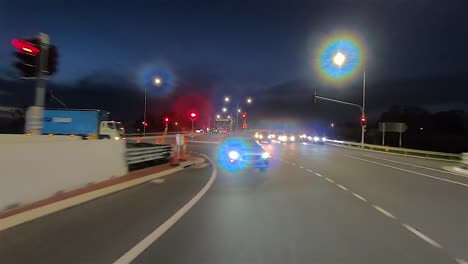 punto de vista de conducción nocturna mirando hacia atrás para el reemplazo de la pantalla verde de la escena interior del automóvil: girar a través de una intersección principal bien iluminada con semáforos