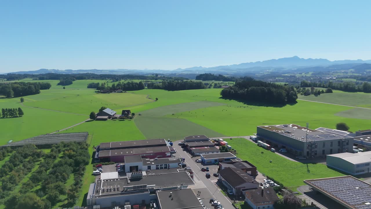 Industrial district of Swiss town with warehouses and parking cars at sunny day. Green fields, forest and all mountains in background. Aerial panorama view
