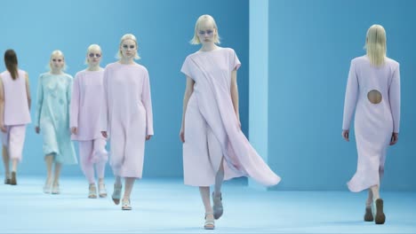 a captivating fashion display: models gracefully showcase elegant pastel attire against a striking blue background, merging style and artistry in a contemporary runway presentation