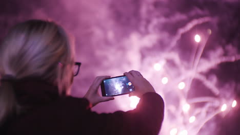 a woman shoots fireworks on a smartphone the lights are beautifully reflected in her glasses slow mo