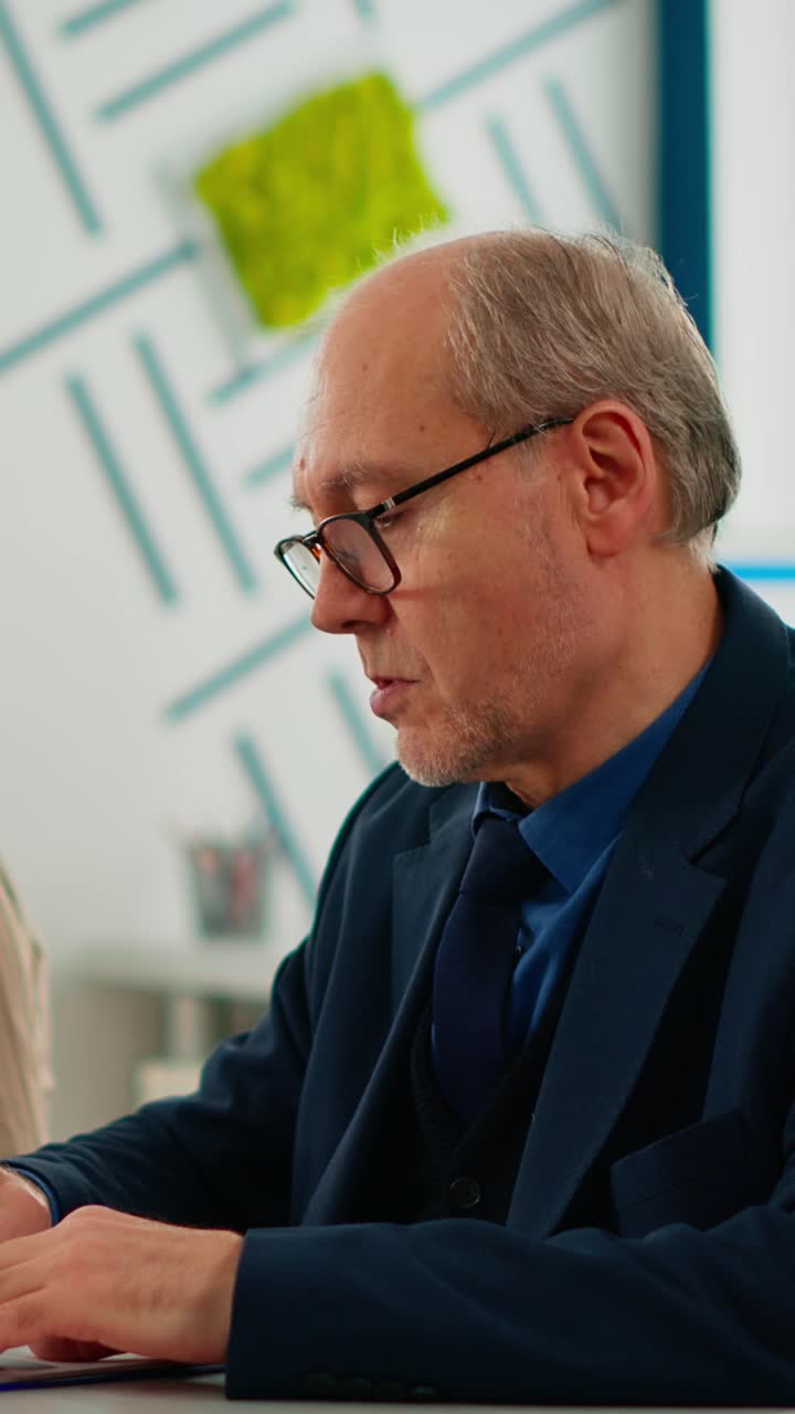 Vertical video Elderly businessman looking at camera smiling sitting in brainstorming room