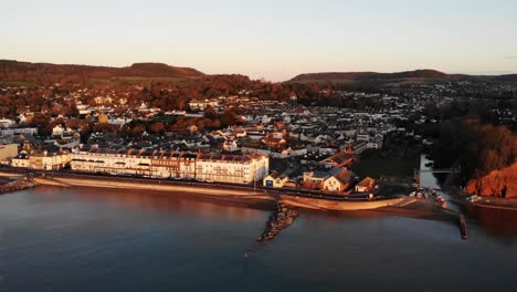 Antenne-Der-Stadtpromenade-Von-Sidmouth,-Die-In-Goldenes-Sonnenaufgangslicht-Getaucht-Ist