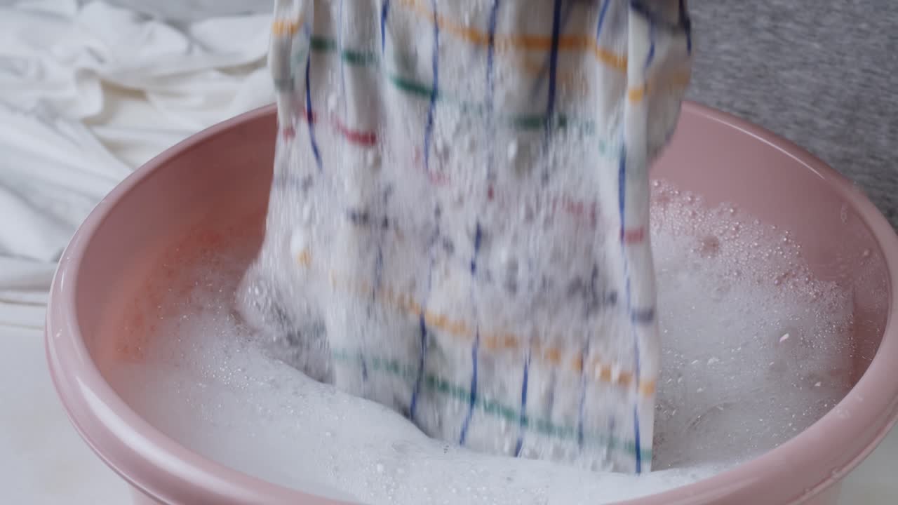 Close-up van handen die stof met de hand wassen in zeepwater