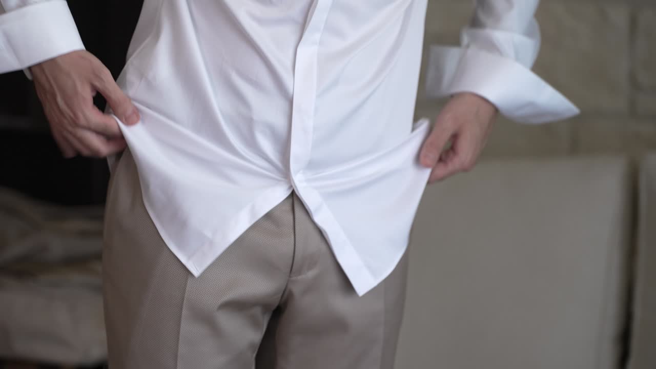Un uomo si trova in una stanza luminosa e inizia ad abbottonarsi la camicia bianca. Si prepara per la giornata concentrandosi su quello che sta facendo. La luce del mattino illumina lo spazio.