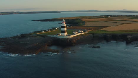 Luftaufnahme,-Sonnenaufgang,-Schwenk-Nach-Links,-Hook-Lighthouse-Befindet-Sich-Auf-Hook-Head-An-Der-Spitze-Der-Hook-Halbinsel-In-Co.-Wexford,-Irland,-ältester-Leuchtturm-Der-Welt,-Wurde-Im-12.-Jahrhundert-Erbaut