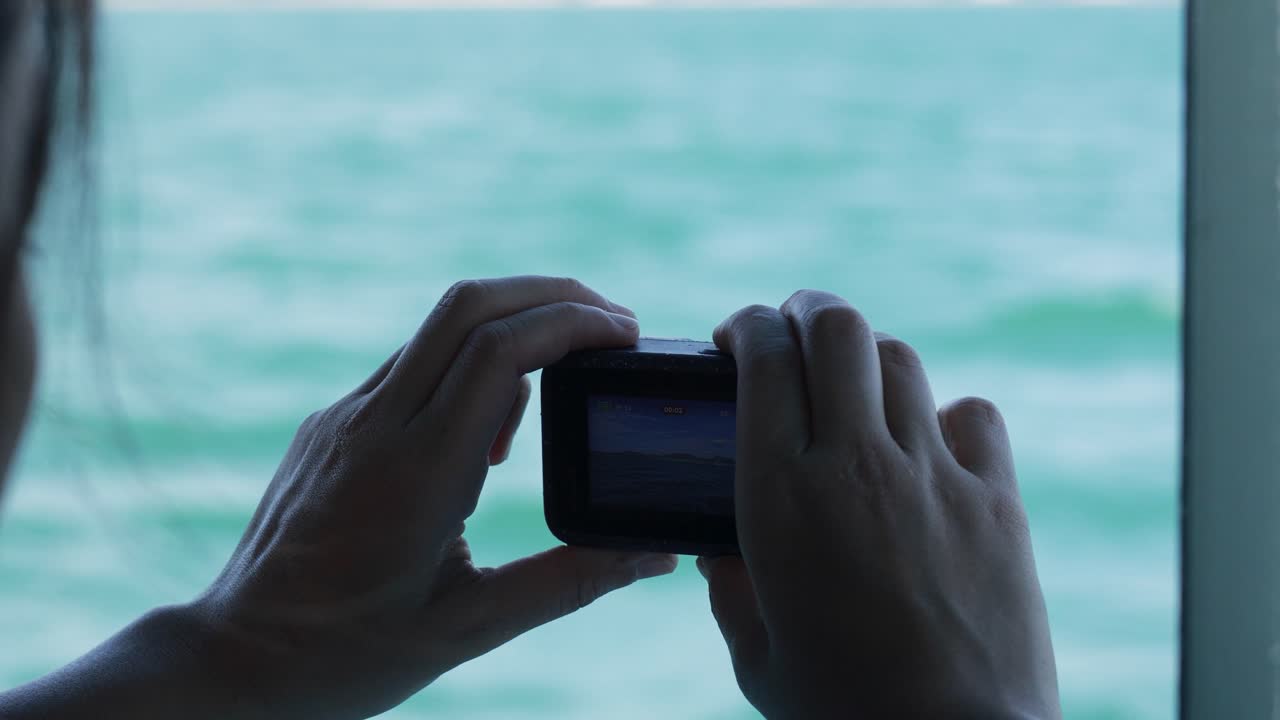 Hands holding a GoPro camera, filming the ocean from a boat in Phuket, Thailand. Calm, serene atmosphere with natural lighting