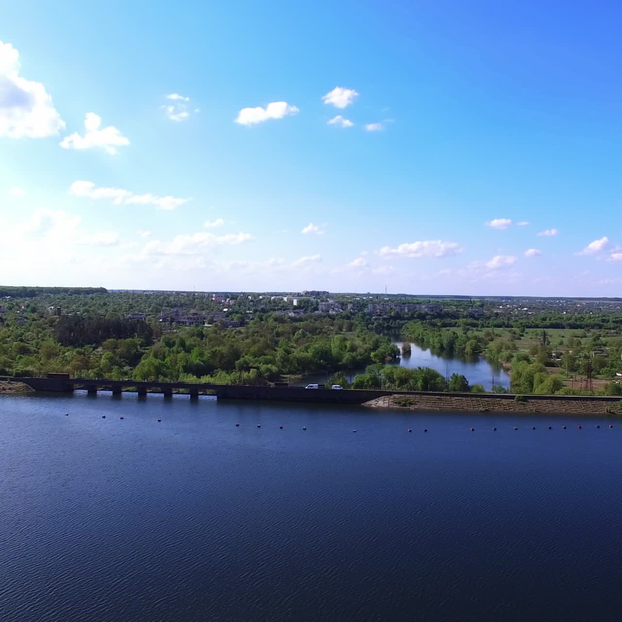 Beautiful blue river with the waterfront and road going along. Private houses scattered among the abundant greenery at the backdrop of blue sky