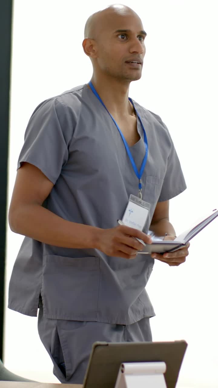 Video verticale: Medico in camice che guarda un collega, posiziona un tablet su un supporto al tavolo e prende appunti.