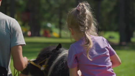 Mädchen-Reitet-Gehorsames-Pony-Mit-Lehrer-über-Grünen-Rasen