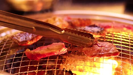 tongs flipping meat on a barbecue grill