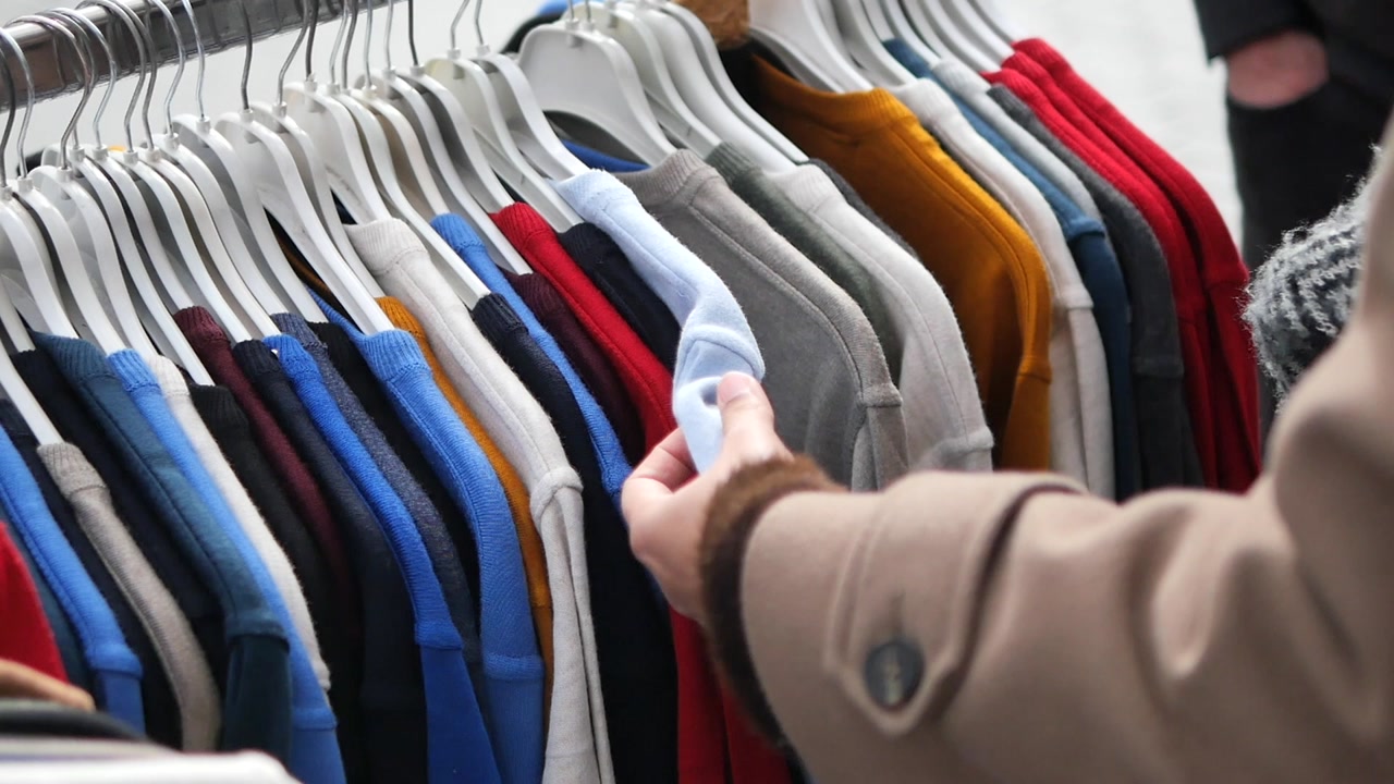 Person's Hand Browsing Colorful Clothes on a Rack in a Store