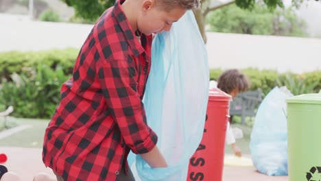 video of caucasian schoolboy collecting rubbish for recycling in schoolyard, copy space