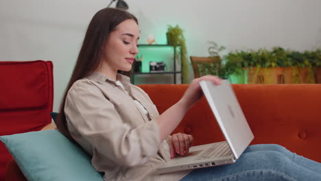 Young-woman-freelancer-sitting-on-couch-closing-laptop-pc-after-finishing-work-in-room-at-home