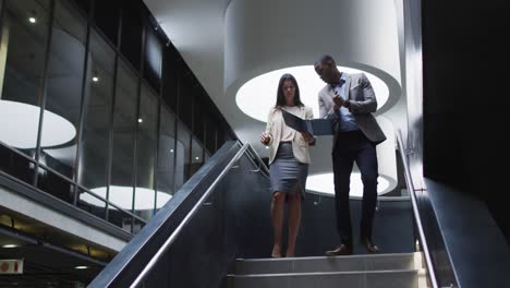 diverse businessman and businesswoman talking and talking down stairs of modern office