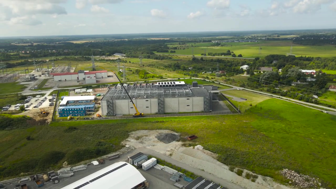 Ampia ripresa aerea che mostra un edificio di data center su larga scala durante la sua fase di costruzione, con una gru in loco e sistemi di raffreddamento HVAC in fase di installazione sul tetto vicino a una centrale elettrica.