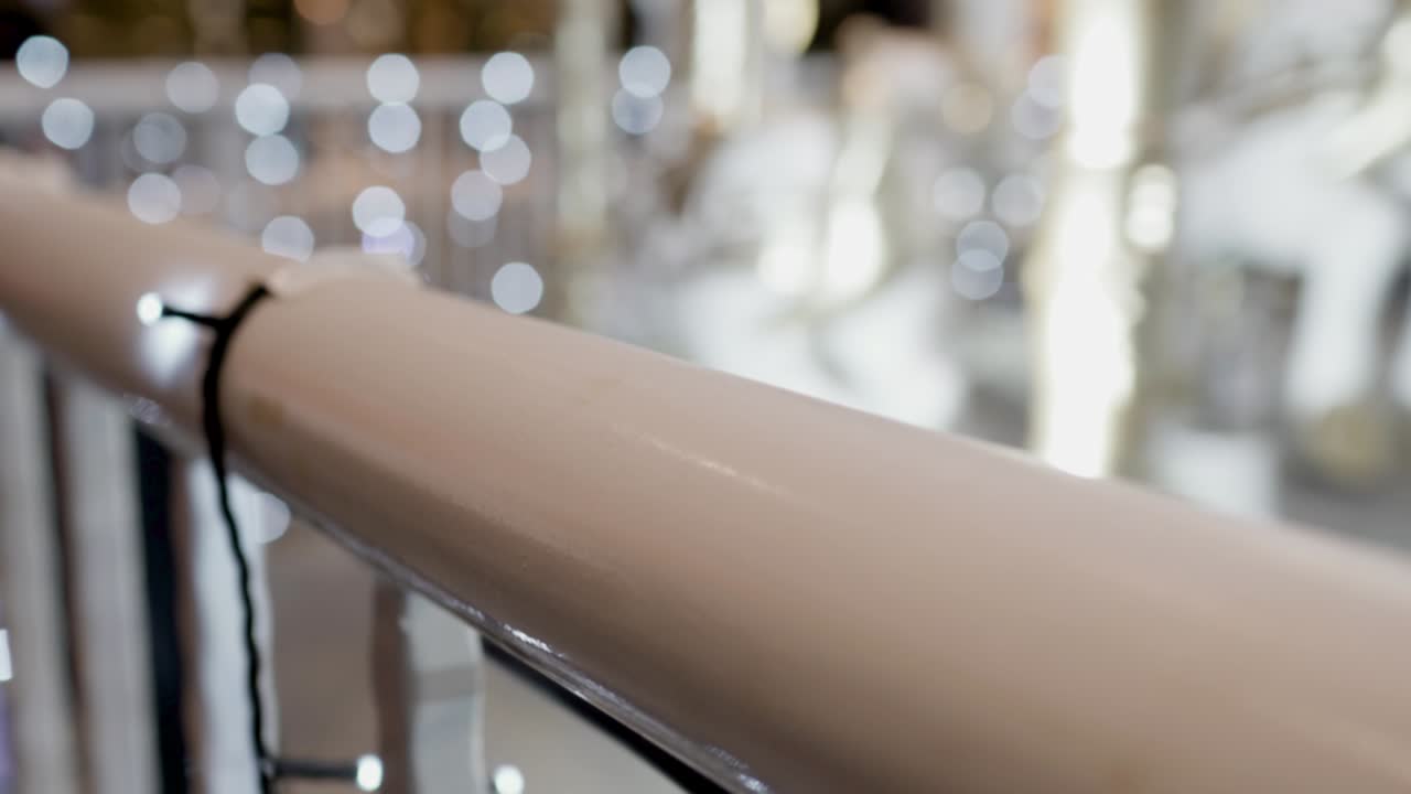 밤에 놀이 공원에서 회전하는 카루셀: 초점은 앞쪽에 있고 배경은 흐릿합니다. 초점은 금속 레일링에 있습니다. 카루셀은 오른쪽에 있습니다.