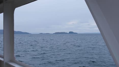 Looking-out-of-passenger-ferry-towards-rocky-and-rugged-landscape-of-Isle-of-South-Uist-and-ocean-in-Outer-Hebrides-of-Scotland-UK