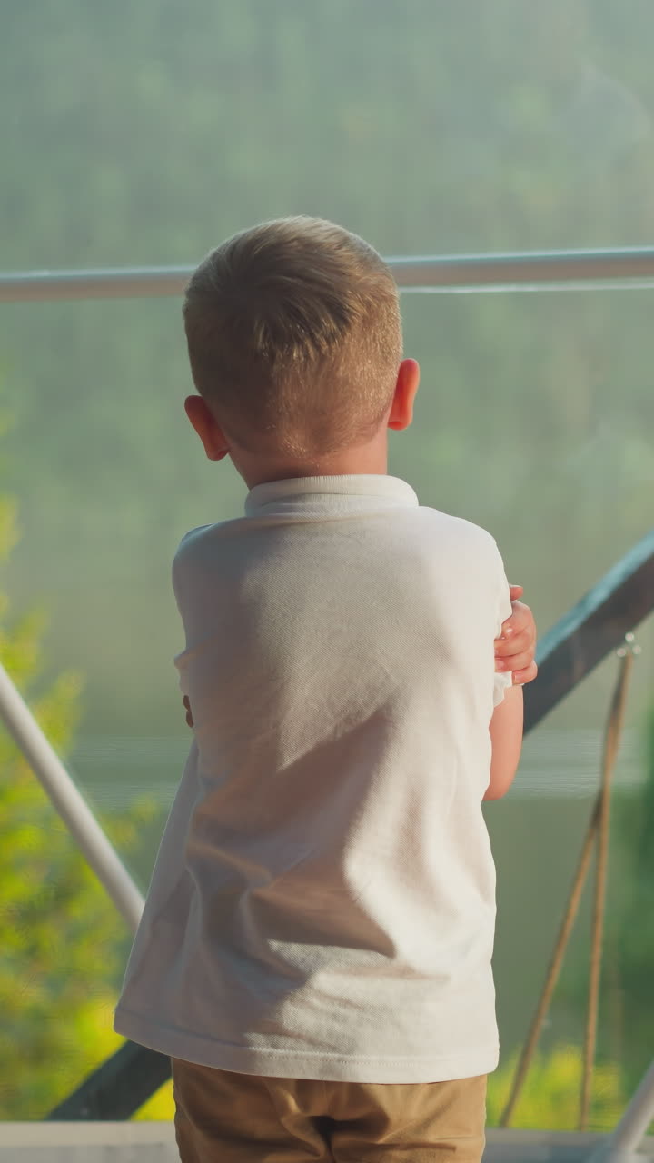 ребёнок стоит в палатке и смотрит на озеро на расстоянии. задумчивый ребенок в белой рубашке размышляет о природе сзади на размытом фоне. спокойный мальчик отдыхает один на рассвете