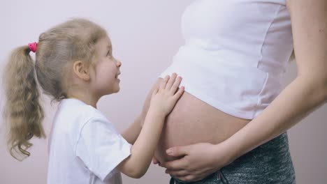 girl touches pregnant mummy large tummy near light wall