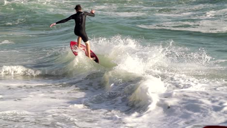 joven surfista skimboarder montando en una ola en cámara lenta en la playa durante la puesta de sol