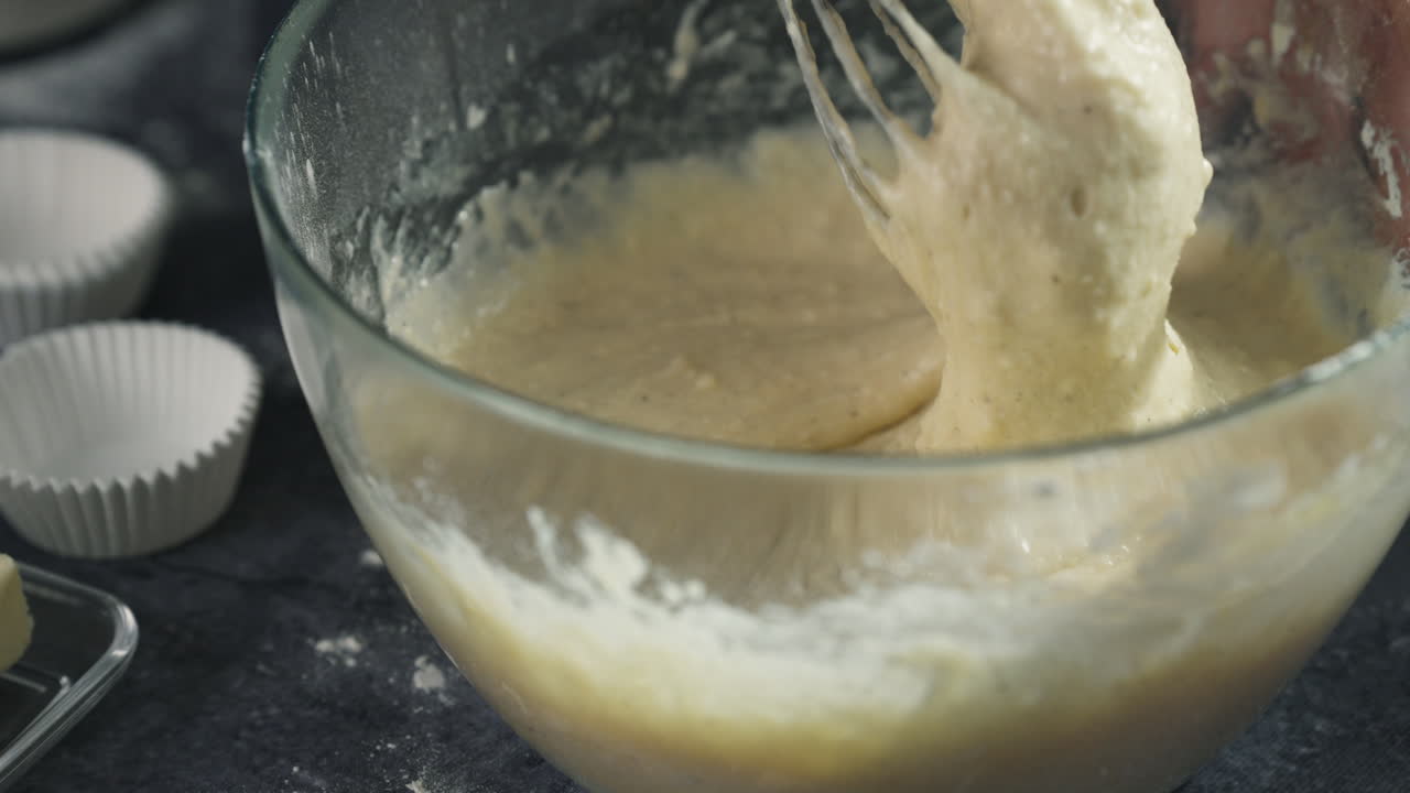 Creaming butter and sugar for cupcake batter during the initial baking steps, batter mixes and thickens as baker checks consistency by raising whisk utensil