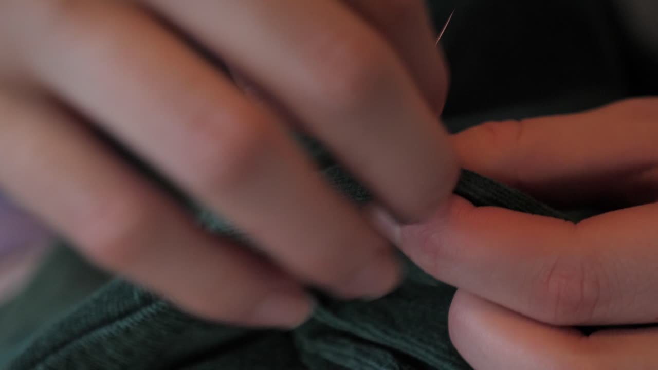 여성의 손은 얇은 금속 바늘과 끈 실로 녹색 재킷 재료를 바느질하여 변경 및 맞춤 조정을 만들고, 매크로의 전면은 바느질로 주변에 도달하는 보기를 닫습니다.