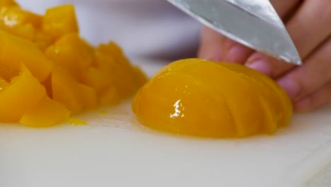 close up of cutting pickled peaches on white cutting board with stainless steel knife