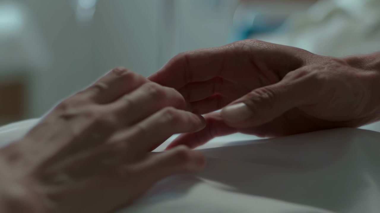 Mani di un operatore sanitario bianco che conforta il paziente, illuminazione soffusa accanto al letto, delicato e lento tocco palmo a palmo.