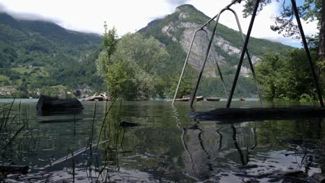 toma en ángulo bajo de un columpio abandonado e inundado en un parque infantil en suiza frente a una gran montaña con una cascada gigante