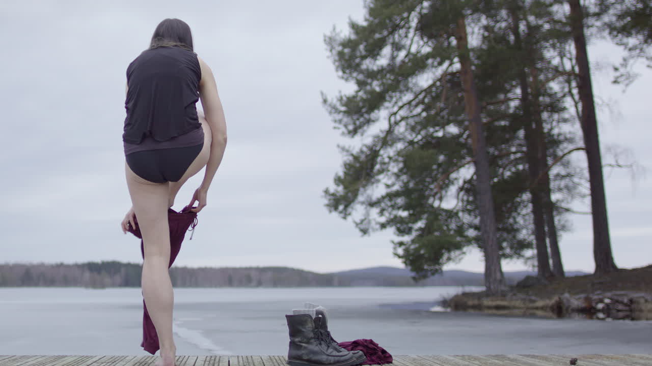 한 여자 가 얼음 목욕 을 준비 하기 위해 옷 을 벗고 있다