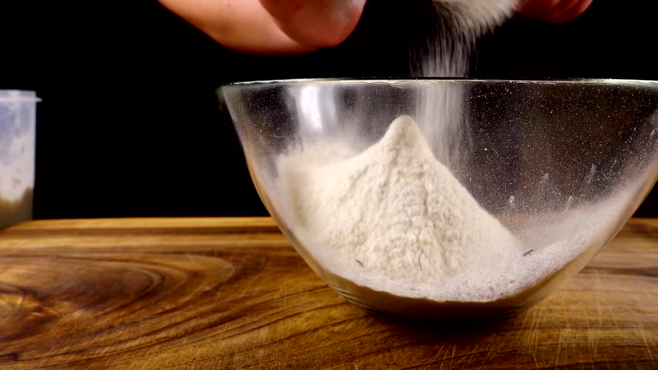 Mengayak tepung menggunakan saringan ke dalam mangkuk kaca di dapur.