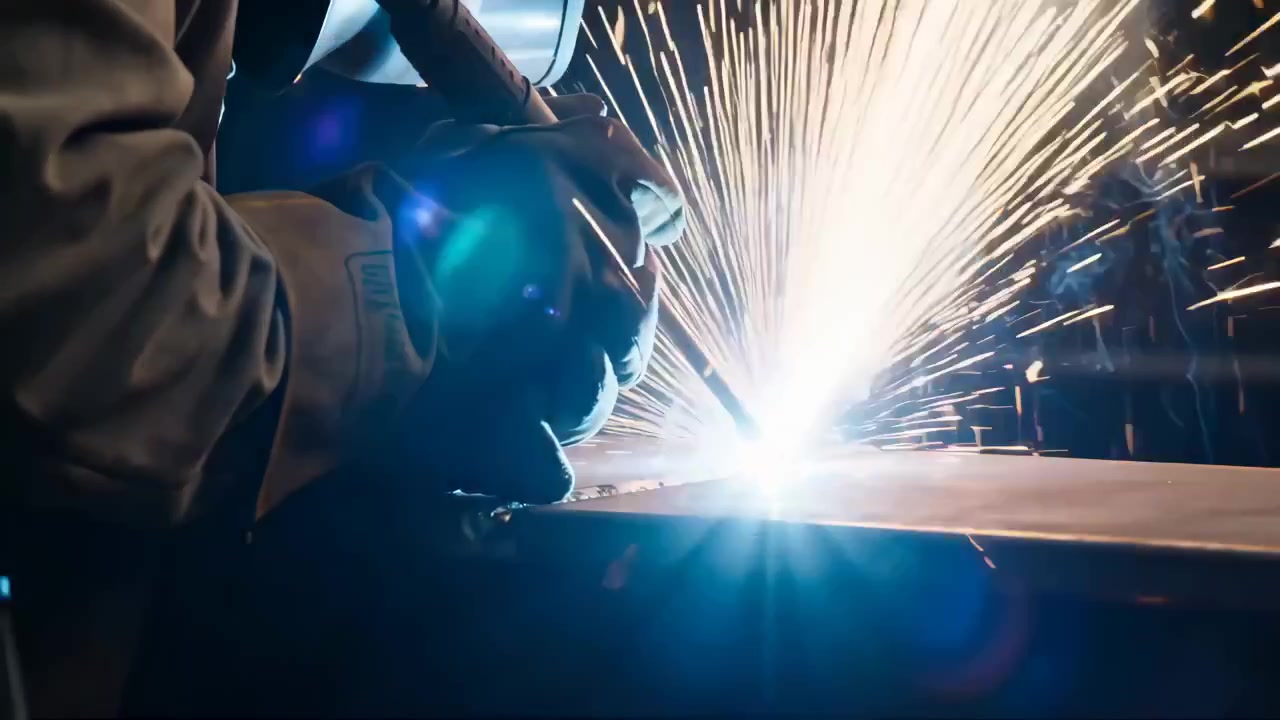 Gloved hands guide welding torch over steel plate, creating intense white-blue arc, cascading amber sparks, molten glow, protective gear, and rugged industrial fabrication detail, with welding, torch