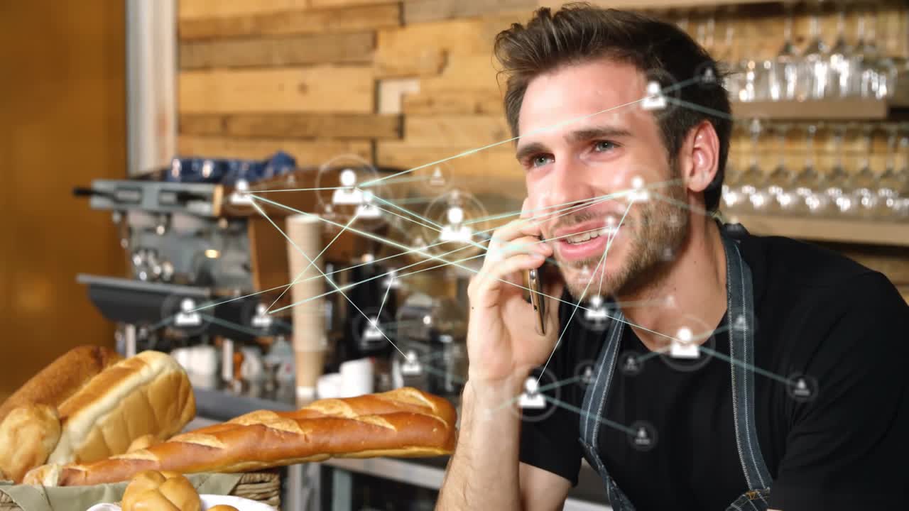 Bäcker hält Smartphone und generiert Netzwerksymbole, die sich um die Bäckertheke ausbreiten, in einer Tech-Demo.